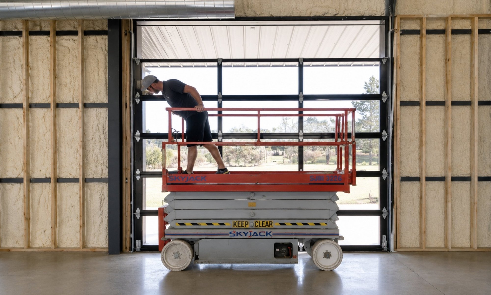 Technician installing a full-view commercial overhead door using a scissor lift inside a warehouse.