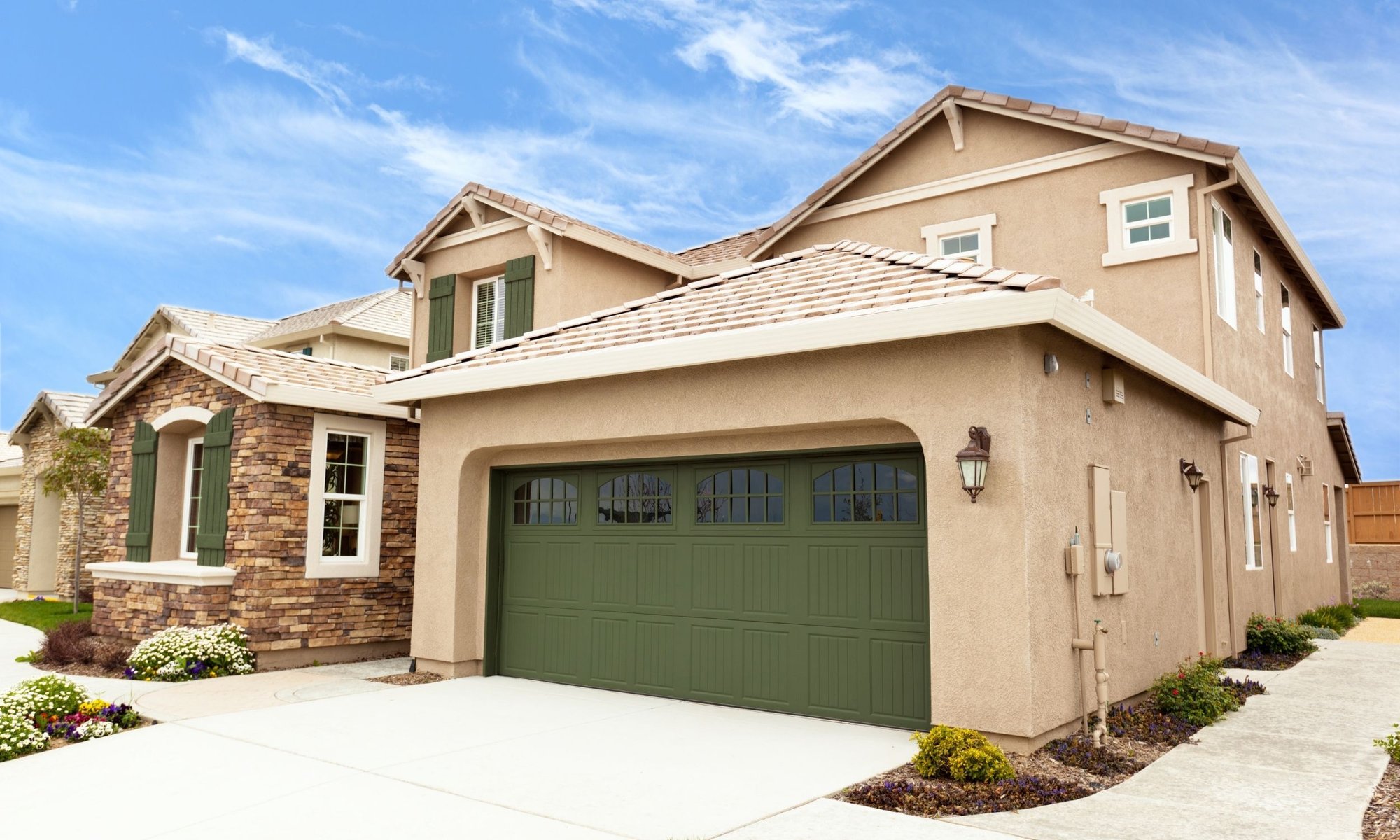 Green carriage-style garage door with decorative windows installed on a modern stucco home.