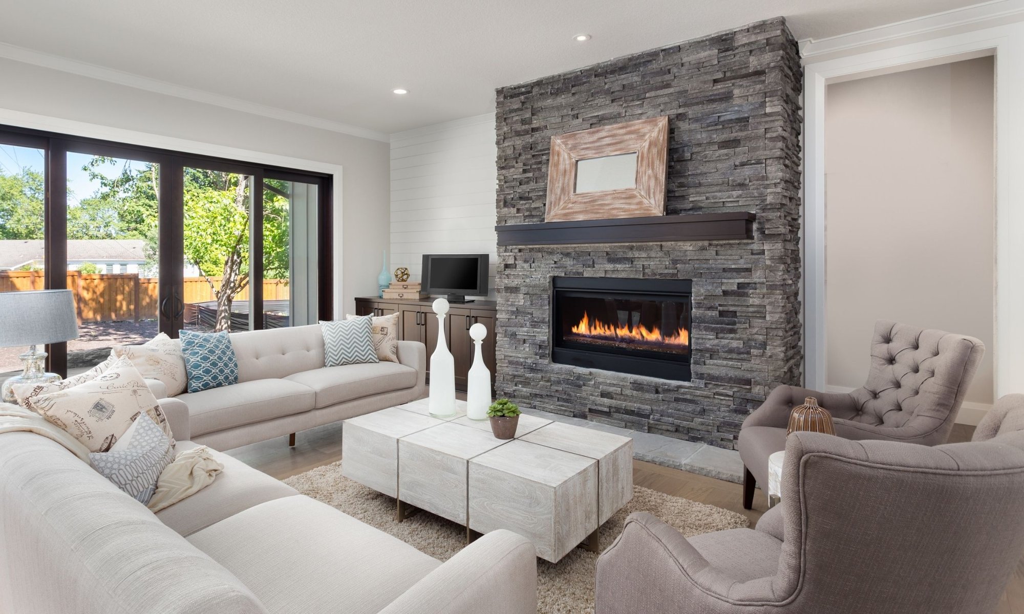 Modern linear gas fireplace with a dark stacked stone surround and wood mantel in a contemporary living room.